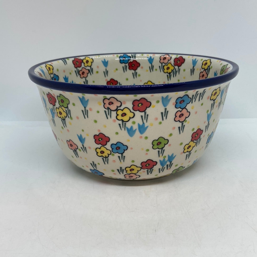 Straight-on side profile of a Ceramika Artystyczna Polish pottery deep round bowl featuring a dark blue rim and hand-painted multi-colored spring flowers on the exterior.