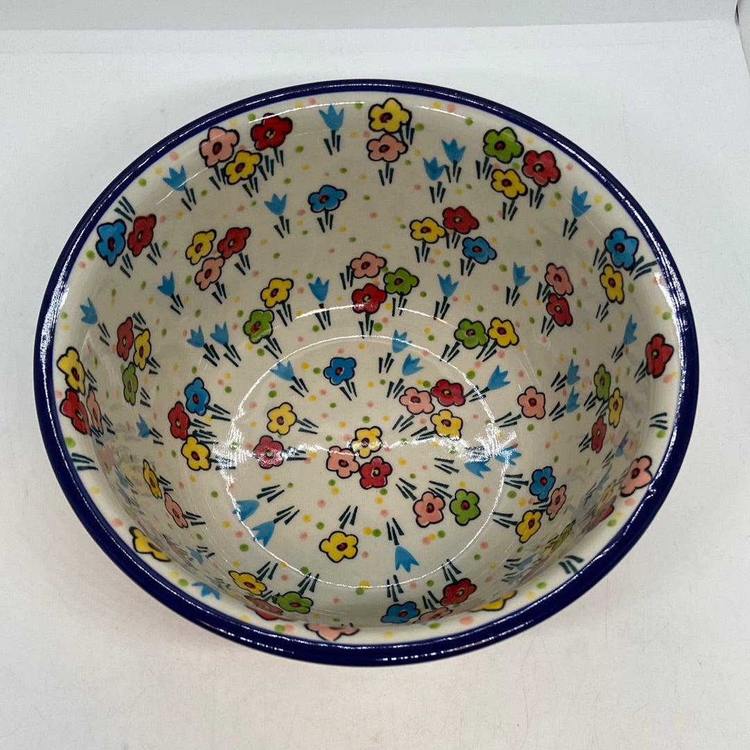 High-angle top-down view looking into a Ceramika Artystyczna Polish pottery deep round bowl, showing a solid dark blue rim and a fully decorated interior basin featuring hand-painted multi-colored spring flowers.
