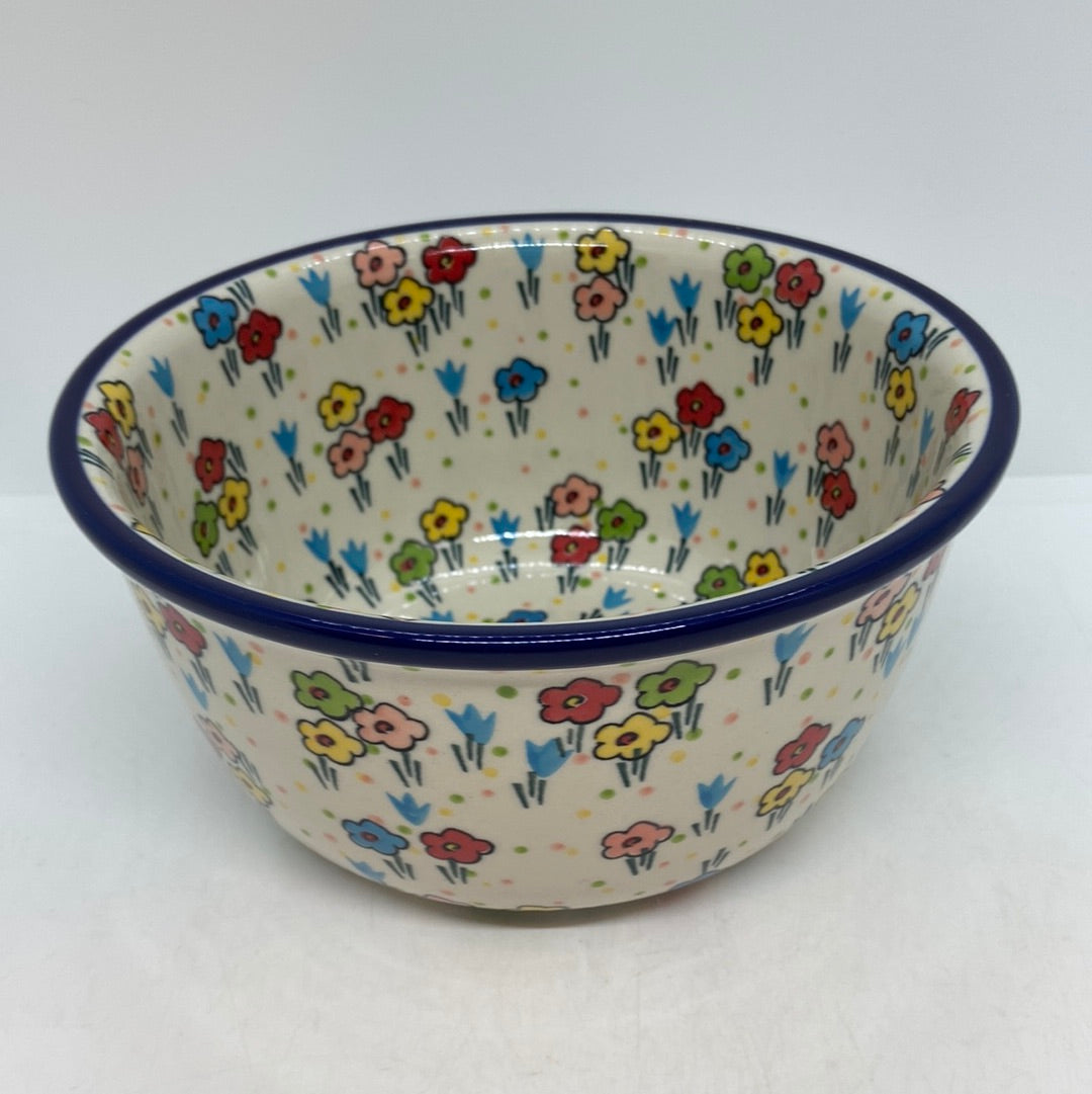Slightly elevated angled view of a Ceramika Artystyczna Polish pottery deep round bowl, showing a dark blue rim and hand-painted multi-colored spring flowers covering the interior basin and exterior walls.