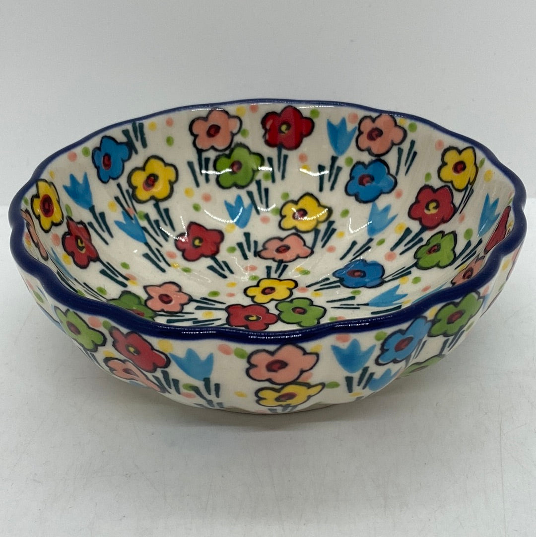 Slightly elevated view of a Ceramika Artystyczna Polish pottery bowl featuring a dark blue scalloped rim and hand-painted multi-colored spring flowers on both the interior and exterior walls.