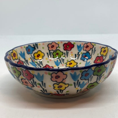 Straight-on side profile of a Ceramika Artystyczna Polish pottery bowl showing a dark blue scalloped rim and a continuous wrap of hand-painted multi-colored spring flowers on the fluted exterior.
