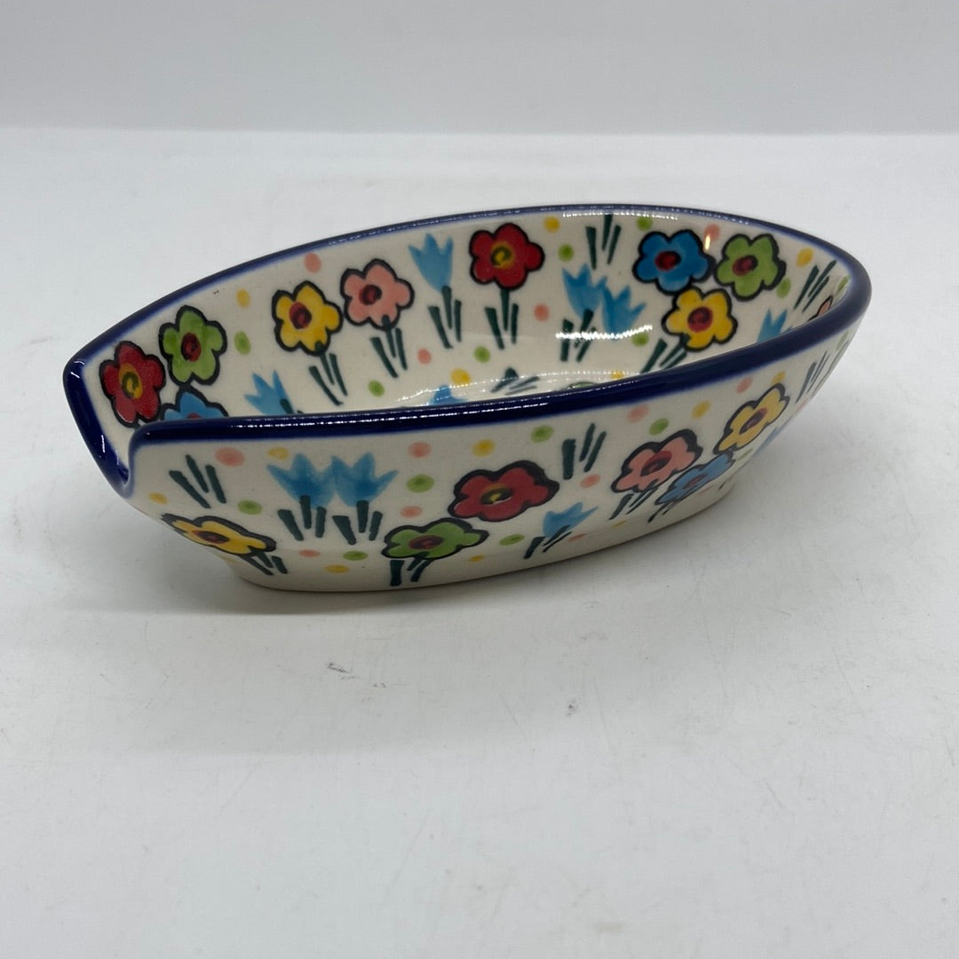 Elevated side view of a Ceramika Artystyczna Polish pottery spoon rest highlighting the U-shaped handle notch, featuring a dark blue rim and hand-painted multi-colored spring flowers.