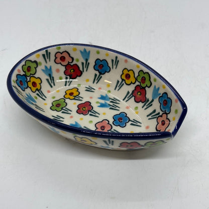 Elevated angled view of a Ceramika Artystyczna Polish pottery teardrop-shaped spoon rest, showing a dark blue rim, a handle notch, and hand-painted multi-colored spring flowers covering the interior and exterior