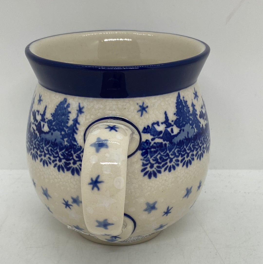 Straight-on view focusing on the patterned handle of a Ceramika Artystyczna Polish pottery bubble mug, flanked by a winter village, falling stars, and a solid dark blue rim.