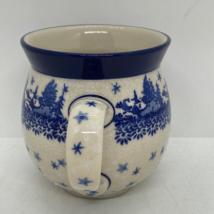 Straight-on view focusing on the patterned handle of a Ceramika Artystyczna Polish pottery bubble mug, flanked by a winter village, falling stars, and a solid dark blue rim.