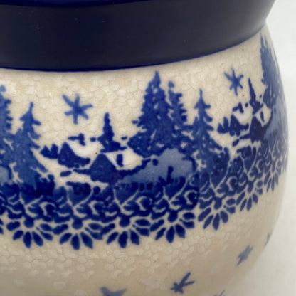Macro close-up view of a Ceramika Artystyczna Polish pottery bubble mug, showcasing a hand-stamped winter village with blue houses, pine trees, a floral border, and a solid dark blue rim.