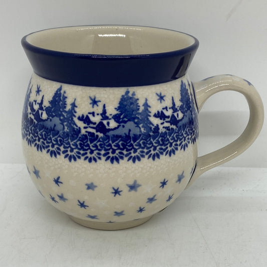 Straight-on side profile of a Ceramika Artystyczna Polish pottery bubble mug with the handle on the right, featuring a hand-painted winter village with blue houses, pine trees, stars, and a solid dark blue rim.