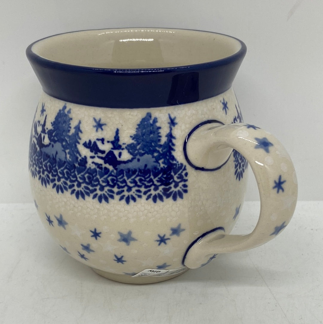 Three-quarter view of a Ceramika Artystyczna Polish pottery bubble mug with a right handle, featuring a hand-painted blue winter village, stars, and a solid dark blue rim.